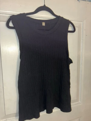 Svart ribbad ärmlös topp kay/day - En svart ribbad topp i ärmlös modell med rund halsringning från kay/day. Toppen är stickad i ett mjukt material och har en enkel, clean look som passar till många olika outfits. Perfekt för lager-på-lager eller att bära som den är. Kommer även att sälja tillhörande mjukisbyxor separat.