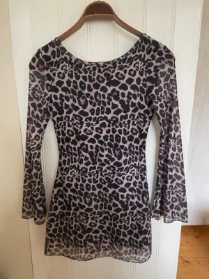 Leopardmönstrad meshklänning - Säljer en kort, figurnära klänning i mesh med leopardmönster. Klänningen har långa ärmar och en snygg rundad ringning både fram och bak. Färgerna går i svart och beige, vilket ger en cool och trendig look.