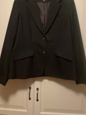 Svart kavaj med diskreta ränder H&M - Säljer en svart kavaj från H&M i storlek 46. Kavajen har diskreta tunna ränder, klassisk krage och två knappar framtill. Fodrad insida och två fickor med lock. 