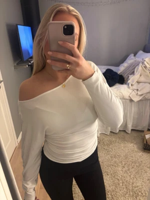 Vit offshoulder långärmad topp - Säljer en vit långärmad topp med offshoulder-design. Toppen är figurnära och har en stilren look med enkel rund halsringning. Materialet känns mjukt och stretchigt, perfekt för att skapa en clean och snygg outfit.