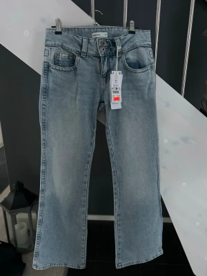 Y2K ljusblå jeans med raka ben - Säljer ett par ljusblå Y2K-inspirerade jeans från Perfect Jeans i storlek 34. Jeansen har raka ben, klassisk femficksdesign och snygga bakfickor med lock och knapp. Tillverkade i jeansmaterial och har en normal passform och låg midja. Perfekta för en trendig vardagslook.