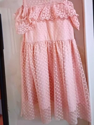 Ljusrosa prickig volangklänning - Supersöt ljusrosa klänning med prickigt mönster och volangdetaljer upptill. Klänningen har en luftig passform och är ärmlös, perfekt för varma dagar. Materialet känns lätt och flowy, och den har en romantisk vibe.