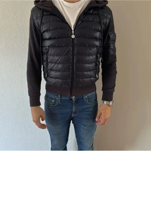 Svart pufferjacka från Moncler S - Säljer en svart pufferjacka från Moncler i storlek S. Jackan har glansig quiltad framsida, huva och dragkedja. Ärmarna är i mjuk bomull och på ena ärmen finns en ficka med Moncler-logga. Perfekt för dig som vill ha en stilren och sportig look.