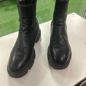 Svarta chelsea boots från CPHGN - Chunky svarta chelsea boots från CPHGN i mjukt skinn med elastiska paneler på sidorna och grov sula. Klassisk rund tå och dragflik bak för enkel påtagning. Perfekta för dig som vill ha en stilren men edgy look.