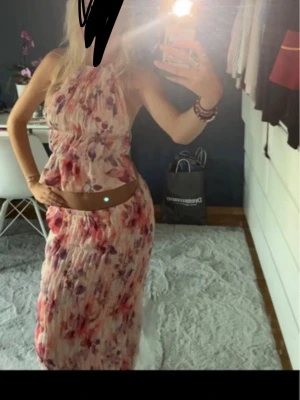 Lång blommigt set i pastellfärger - Säljer ett långt, plisserad set  med blommigt mönster i rosa, lila och röda toner. Kjolen har en mjuk, flowy känsla. Perfekt för sommarens alla tillfällen och ger en romantisk vibe.