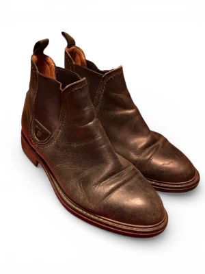 Bruna chelsea boots från Gant - Säljer ett par klassiska bruna chelsea boots från Gant i skinn. Skorna har rund tå, elastiska paneler på sidorna och dragflikar både fram och bak. Snygg kontrastsula och diskret Gant-logga på sidan. Perfekta till jeans eller chinos.