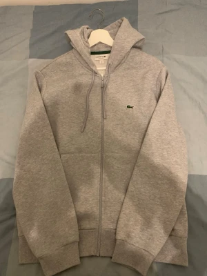 Lacoste Zip Hoodie  - Lacoste Grå Zip up hoodie i storlek L. Classic fit, nästan helt oanvänd, används en gång och har inga tecken på smuts eller slitage. Väldigt bra passform och kvalité på tröjan. 