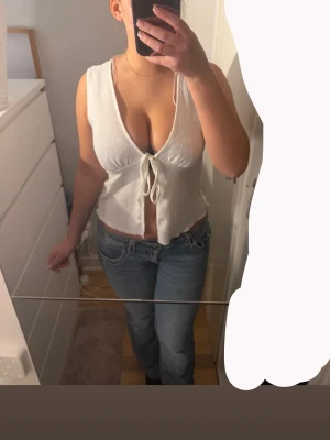 Vit ribbad linnetopp med knyt - Säljer en vit ribbad linnetopp med djup v-ringning och knyt framtill. Toppen är ärmlös och croppad, perfekt för varma dagar eller lager på lager. Enkel och stilren design som passar till mycket.