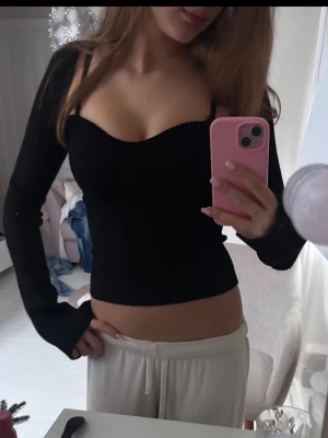 Svart ribbad långärmad topp - Säljer en svart ribbad topp med lång ärm och figurnära passform. Toppen har en snygg sweetheart-urringning och är stretchig, vilket gör den riktigt bekväm. Perfekt att styla med både jeans och kjol för en trendig look.