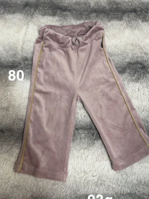  mjukisbyxor med snörning - Säljer ett par mjukisbyxor i mjukt material med snörning i midjan och guldig dekorativ linje längs sidorna. Byxorna har en loose passform och är perfekta för chill dagar. Supersköna och stilrena för dig som gillar bekväma kläder.🌸 Fint använt skick. Storlek 80
