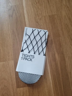 Svarta nätleggings - Säljer ett par svarta nätleggings med grovt fisknätsmönster. Perfekta att styla under kjol eller shorts för en edgy look. Tightsen är elastiska och sitter tajt mot benen.