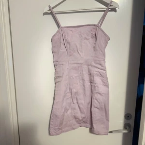 Ljuslila kort jeansklänning  - Säljer en ljuslila kort jeansklänning med smala axelband och figurnära passform. Klänningen har en synlig dragkedja i ryggen. Klänningen bör storlek L men skulle säga att den passar en S och M också. Lite liten för mig och jag har M 