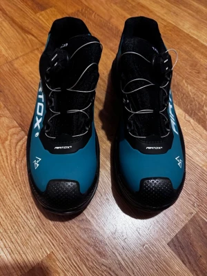 AIRTOX TX33 sneakers med snabbsnörning - Säljer ett par AIRTOX TX33 sneakers i svart och petrolblått med vit logga på sidan. Skorna har snabbsnörning med wire och robust tåparti. Ovandelen är i syntetmaterial och designen är sportig och modern. Perfekta för dig som gillar techiga detaljer och cool look.
