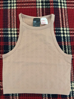 Beige ribbad linnetopp från H&M - Säljer en beige linnetopp från H&M i storlek S. Toppen är ribbad med små diskreta prickar i mönstret och har en ärmlös design med breda axelband. Materialet är mjukt och stretchigt, perfekt för en chill och enkel look.