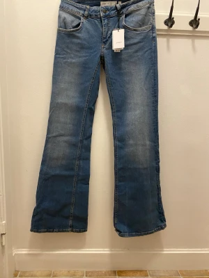 Blå bootcut jeans från Subdued - Säljer ett par blå bootcut jeans från Subdued i storlek 38 (eu) eller då 42 (italiensk storlek). Jeansen har snygga stjärndetaljer med nitar på bakfickorna och klassisk femficksdesign. Tillverkade i stretchigt jeansmaterial med normal passform och låg midja. Perfekta för en cool och avslappnad stil. De är i nytt skick och alltså oanvända. Köpte för 908 kr.