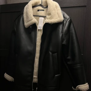 Svart fodrad skinnjacka från Gina Tricot - Säljer en svart skinnjacka från Gina Tricot i storlek S. Nypris 899:-. Jackan har mjukt, krämvitt teddyfoder på insidan och krage, samt detaljer vid ärmslut. Yttermaterialet är slätt och i syntet med dragkedja framtill. Helt ny, prislappen kvar. Säljer eftersom jag inte gillade passformen på mig. 