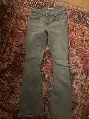 Grå bootcut jeans - Säljer ett par gråa jeans med bootcut-snitt. Byxorna har klassisk femficksdesign och är tillverkade i jeansmaterial. Passar dig som gillar en lite vidare passform nedtill och vill ha en stilren look.