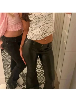 Svarta bootcut byxor i skinnimitation - Säljer ett par svarta byxor i skinnimitation med bootcut passform. Byxorna har låg midja och stängs med dragkedja. Byxorna är slutsålda och säljs inte längre! De är även gasta strechiga med ett skönt material på insidan! 