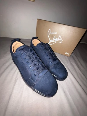 Mörkblå sneakers från Christian Louboutin - Snygga mörkblå sneakers från Christian Louboutin i mocka med ikonisk röd sula och broderad logga på hälen. Skorna har rund tå, platt sula och klassisk snörning. Perfekta för dig som vill sticka ut med exklusiv stil och detaljer. Storlek 44. Äktenhetsbevis ingår samt alla andra artiklar med på bilderna. Inga defekter eller syntecken på användning därav ett pris på 1999!!