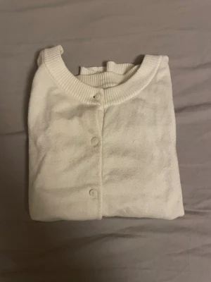 Vit kortärmad kofta från Lindex - Kortärmad kofta från Lindex i mjuk vit bomull. Klassisk rund halsringning och ribbade kanter. Knäpps framtill med fem matchande knappar. Perfekt att slänga över en topp för en clean och enkel look.