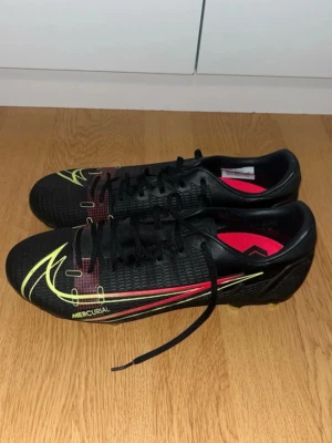 Nike Vapor 14 Academy fotbollsskor storlek 42 - Säljer ett par stilrena Nike Mercurial fotbollsskor i svart med neon-gula detaljer och röd insida. Mercurial-serien är känd för sin lätta vikt, tajta passform och explosiva acceleration – perfekta för snabba spelare på kanten eller i anfall.  Skickas snabbt, hör av dig vid frågor eller om du vill ha fler bilder! 