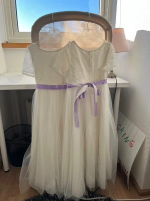 Vit långklänning med spets, utmärkt för brudnäbbar - Säljer två eleganta vita långklänningar med spets upptill och korta ärmar. Klänningarna har ett ljuslila satinband i midjan som kan knytas till rosetter. Satinbanden är ditsydda och går därför utmärkt att ta bort (se sömmen på bild 4). En utav klänningarna har en fläck och ett hål (se bild 5 & 6) och säljs därav något billigare. Tillhörande korg ingår (se bild 7) Hör av er vid intresse, priset kan självklart diskuteras. 