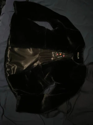 Svart pälsjacka från LingFei Fashion - Säljer en helt oanvänd svart pälsjacka från LingFei Fashion. Jackan har en rak med lite utsväng i slutet passform, långärmade ärmar och är gjord i mjukt fuskpälsmaterial. Den är helsvart och har en enkel, stilren look utan dragkedja men ett litet knäppe högst upp.