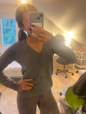 Grå v-ringad tröja från Benetton - Mysig grå v-ringad tröja från Benetton i mjuk ullmix. Klassisk modell med lång ärm och ribbade muddar. Perfekt att slänga på sig när det är kyligt ute. Enkel och stilren design som funkar till det mesta.