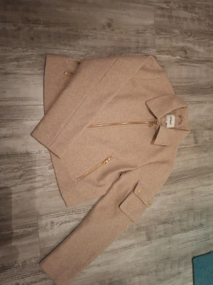 Beige ulljacka med dragkedja -  Beige jacka från Only. Jackan har dragkedja framtill, två fickor med dragkedja och en fickdetalj med knappar på ena ärmen. Storlek M. Jackan är ny och oandvänd, lapp finns ej kvar. Köpt för 499kr, pris kan förhandlas!