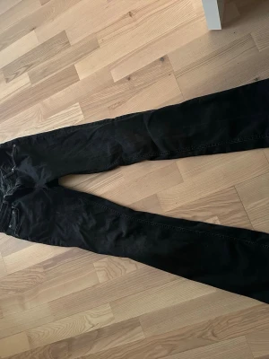 Svarta jeansbyxor med rak passform - Svarta jeansbyxor med klassisk femficksdesign och rak passform. Byxorna har silverfärgade nitar och knapp, samt dragkedja i gylfen. Materialet är jeans och färgen är helsvart, vilket gör dem enkla att matcha med olika stilar.