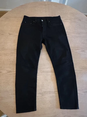 Svarta jeans från Acne Studios - Svarta jeans från Acne Studios med klassisk femficksdesign och diskret logopatch bak i midjan. Jeansen har rak passform och är tillverkade i ett slitstarkt bomullsmaterial med en snygg, mörk ton. Perfekta för dig som gillar stilrena och minimalistiska plagg.