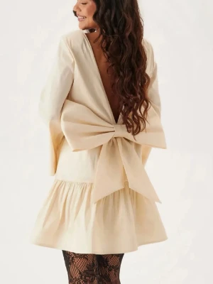 Champagnefärgad miniklänning med rosett Bubbleroom - Supersöt cream kortklänning från Bubbleroom med stor rosett i ryggen och öppen rygg. Den är slutsåld på hemsidan och jag har aldrig använt den. Klänningen har vida långa ärmar och volang nertill. Materialet är glansigt, satin och känns lyxigt, perfekt för nyår!✨