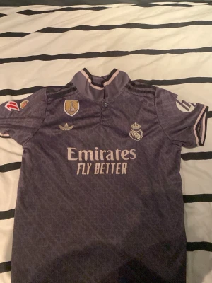 REAL MADRID T-SHIRT - DETTA ÄR EN REAL MADRID TRÖJA SOM BEHÖVER EN NY ÄGARE,DENNA TRÖJA ÄR KÖPTE GANSKA LÄNGE SEN OCH ANVÄNDS INTE MER,DET ÄR EN GRÅ-AKTIG T-SHIRT/TRÄNINGSTRÖJA MED SPELAREN MBAPPÉ MED NUMMER 9. JAG SOM ÄR 175 TYCKER ATT DEN PASSAR VÄLDIGT BRA PÅ MIG DENNA STORLEK SKULLE PASSA FÖR DIG SOM ÄR 160-175