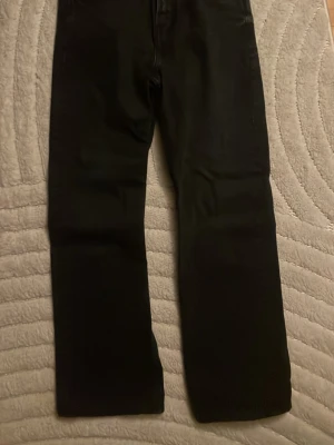 Svarta raka jeans - Säljer ett par svarta jeans med rak passform och klassisk femficksdesign. Byxorna har normal midja och är tillverkade i ett mjukt bomullsmaterial med lite stretch. Perfekta till sneakers eller boots och funkar året runt.