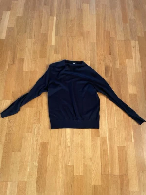 Mörkblå merinoulltröja från Uniqlo - Säljer en stilren mörkblå tröja från Uniqlo i mjuk merinoull. Tröjan har rund hals, lång ärm och en slim passform som sitter snyggt på kroppen. Perfekt till jeans eller chinos för en clean look.