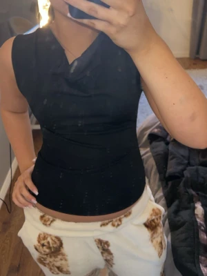 Svart ärmlös topp med draperad hals - Säljer en svart, tight topp med draperad halsringning. Toppen är ärmlös och har en stilren, figurnära passform som framhäver siluetten. Perfekt att matcha med jeans eller kjol för en snygg look. Materialet känns mjukt och stretchigt.