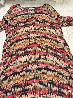 Mönstrad klänning från Masai XXL - Säljer en cool och färgstark klänning från Masai i storlek XXL. Klänningen har ett abstrakt mönster i svart, röd och beige med inslag av brunt. Den har en avslappnad passform och är tillverkad i mjukt material som känns skönt mot huden. Perfekt för dig som gillar unika prints.