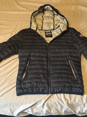 Svart pufferjacka från Colmar - Säljer en svart pufferjacka från Colmar Originals med huva och två dragkedjeförsedda fickor. Jackan har quiltad design och är fodrad i ljusgrått. Perfekt för kyliga dagar och har en clean look med diskret logga på ärmen. PASSAR FOLK SOM ÄR UNGEFÄR 165-180 cm-Passform smal