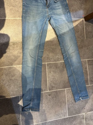 Blå skinny jeans från KRISTEN - Säljer ett par ljusblå skinny jeans från KRISTEN i storlek 26/30. Jeansen har dragkedjor vid bensluten och klassiska kontrastsömmar. Perfekta för dig som gillar en tight passform och vill ha en enkel men snygg look.