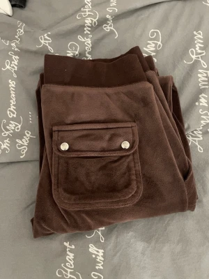 Bruna Juicy Couture mjukisbyxor XS - Bruna mjukisbyxor från Juicy Couture i storlek XS. Är gjorda i mjuk velour. Passformen är loose på mig. och modellen är rak med normal midja. Det saknas snören men dom är fortfarande lika snygga 💕