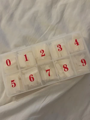  Nageltippar i olika storlekar - Säljer ett set med transparenta nageltippar i en praktisk plastlåda med tio fack, numrerade från 0 till 9. Tipparna är gjorda av plast och finns i flera storlekar för att passa olika naglar. Till för att använda i samband med gele. 