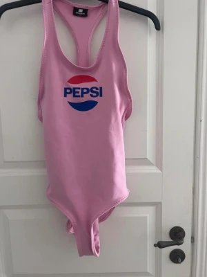 Rosa Pepsi baddräkt - Säljer en rosa baddräkt med Pepsi-logga i blått och rött framtill. 