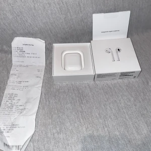 Apple AirPods  - Apple AirPods utan hörlurar. Fungerar med iOS-enheter, Apple Watch och Mac. Originalkartong och kvitto medföljer. Viss smuts och slitage synligt i laddningsetuiet, men produkten är fullt fungerande.