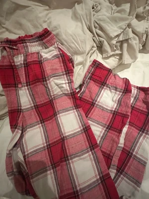 Röd- och vitrutiga mjukisbyxor - Säljer ett par mjukisbyxor med röd och vit rutig design. Byxorna har resår och snörning i midjan för skön passform. Materialet är mjukt och passar perfekt för chill hemma. Mönstret är klassiskt rutigt och färgerna är riktigt poppiga.