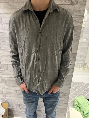 Grå skjorta från Hugo Boss slim fit - Säljer en grå skjorta från Hugo Boss i slim fit-modell. Skjortan har ett diskret fiskbensmönster, klassisk krage och knappar framtill. Långärmad och tillverkad i mjukt bomullstyg som känns skönt mot huden. Perfekt för dig som gillar stilrena och enkla plagg.