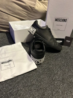 Svarta Moschino skor - Snygga svarta sneakers från Moschino med stor vit logga på hälen, använda cirka 5 gånger pga att de inte passar mig låda och allt medföljer skriv vid prisförslag eller frågor 