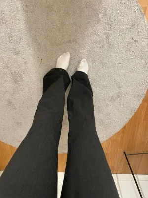 Svarta bootcut byxor - Säljer ett par mörk gråa kostymbyxor med hög midja. Byxorna har en snygg, figurnära passform upptill och släpper ut vid benen för en trendig siluett. Perfekta att styla med crop top eller stickad tröja. Materialet känns mjukt och stretchigt.