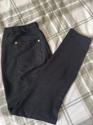 Svarta byxor från Michael Kors, M - Svarta byxor från Michael Kors i storlek M. Byxorna har raka ben, guldiga nitar vid fickorna och är tillverkade i ett bomullsliknande material med lätt struktur. Snygg och enkel design som funkar till många olika stilar.