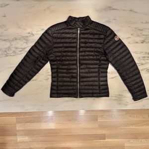 Colmar herrjacka stl 46 (S–M) – svart dunjacka i mycket fint skick - Stilren och lätt dunjacka från Colmar Originals, färg Nero Iron (svart). Klassisk modell utan huva med ståkrage och logga på ärmen. Två fickor med dragkedja. Mycket fint skick, inga fläckar eller skador. Nypris ca 4 000 kr. Passar perfekt för höst/vår – snygg både till vardags och på jobbet.