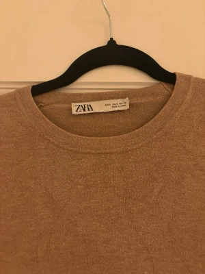 Beige stickad tröja från Zara - Snygg beige stickad tröja från Zara med rund hals och långa ärmar. Tröjan har en slim passform och dekorativa knappar vid ärmsluten som ger en extra detalj. Perfekt för dig som gillar stilrena och enkla plagg.